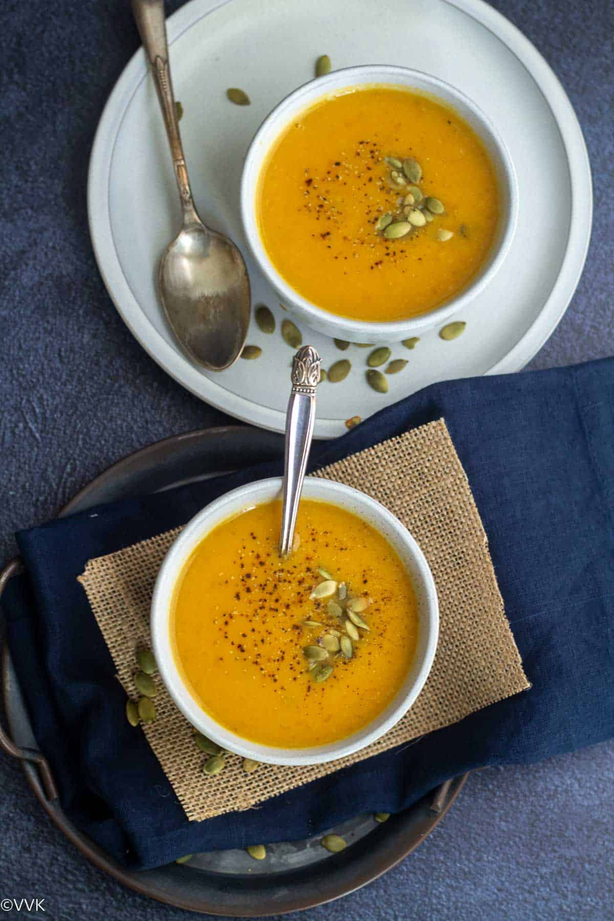overhead shot of pumpkin soup served in two white bowls topped with pumpkin seeds