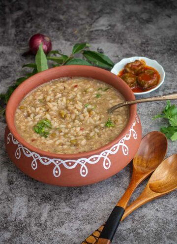 square image of gruel served in clay pot with pickle and other condiments on the side
