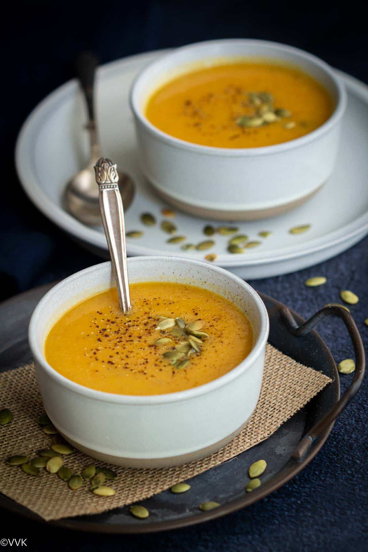 vegan pumpkin soup served in two white ceramic bowls placed on burlap cloth