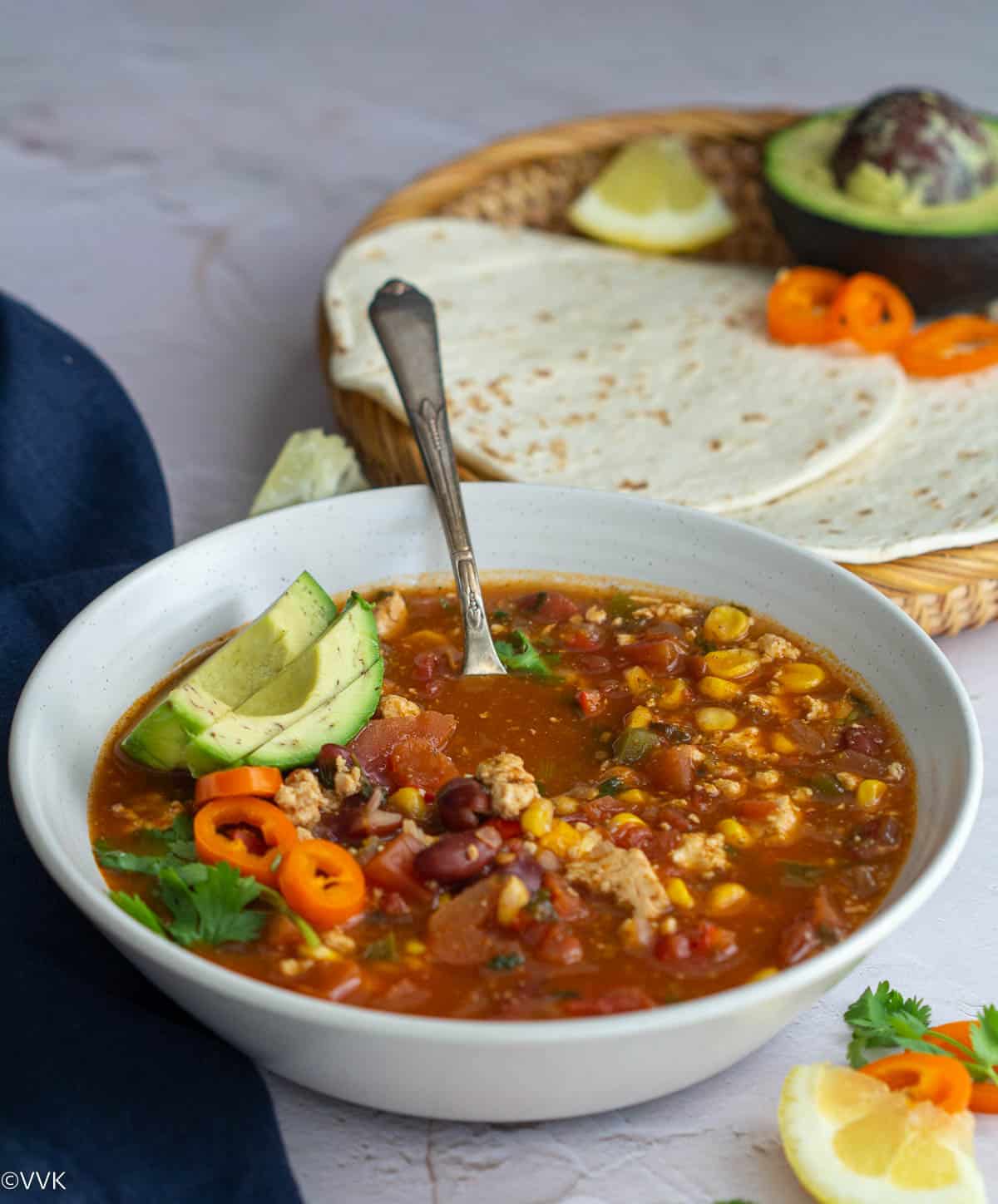 taco soup served in white bowl with tortillas and avocado on the side