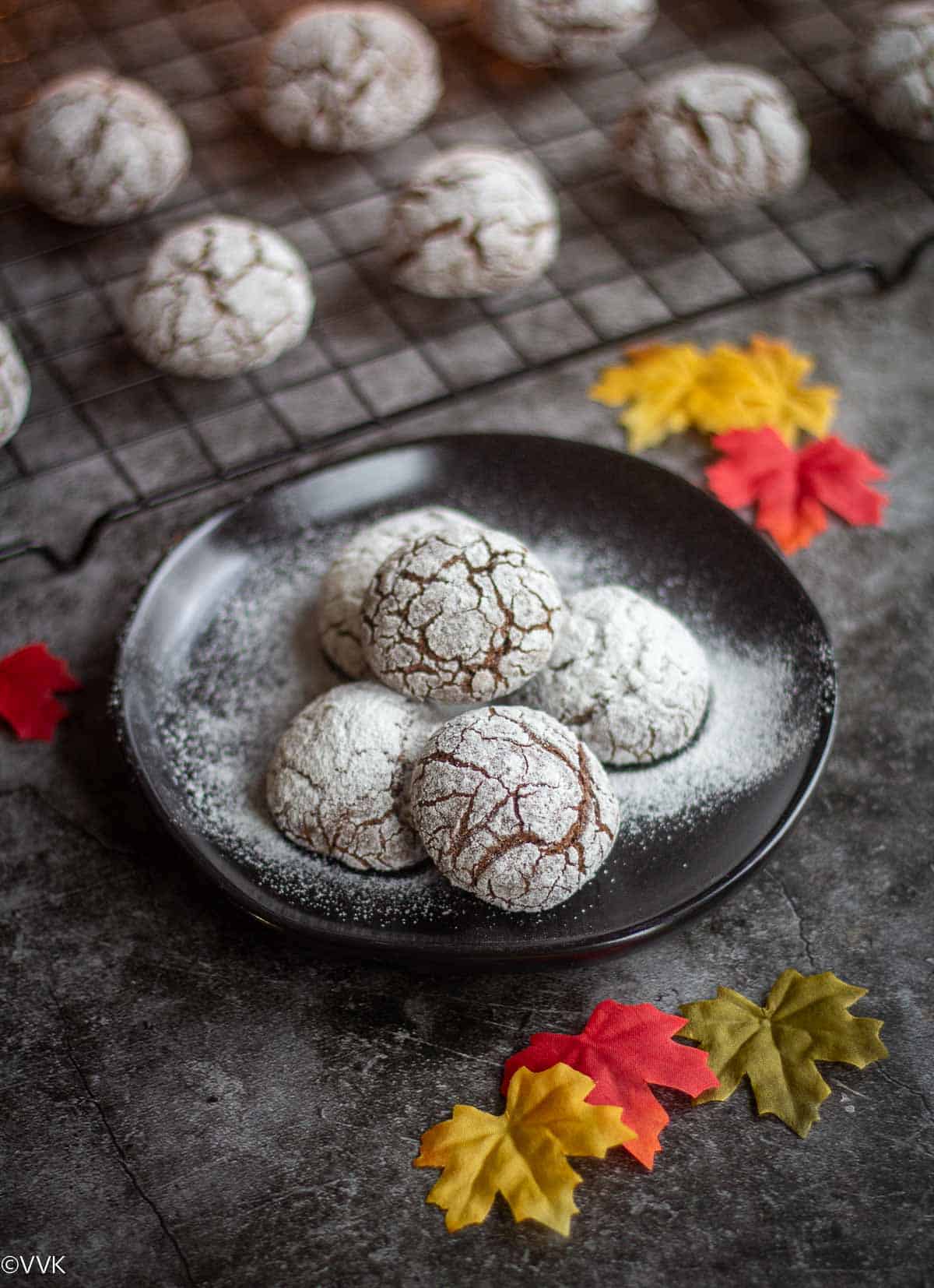 chocolate crinkle cookies placed on cookie rack and black plate with some fall leaves