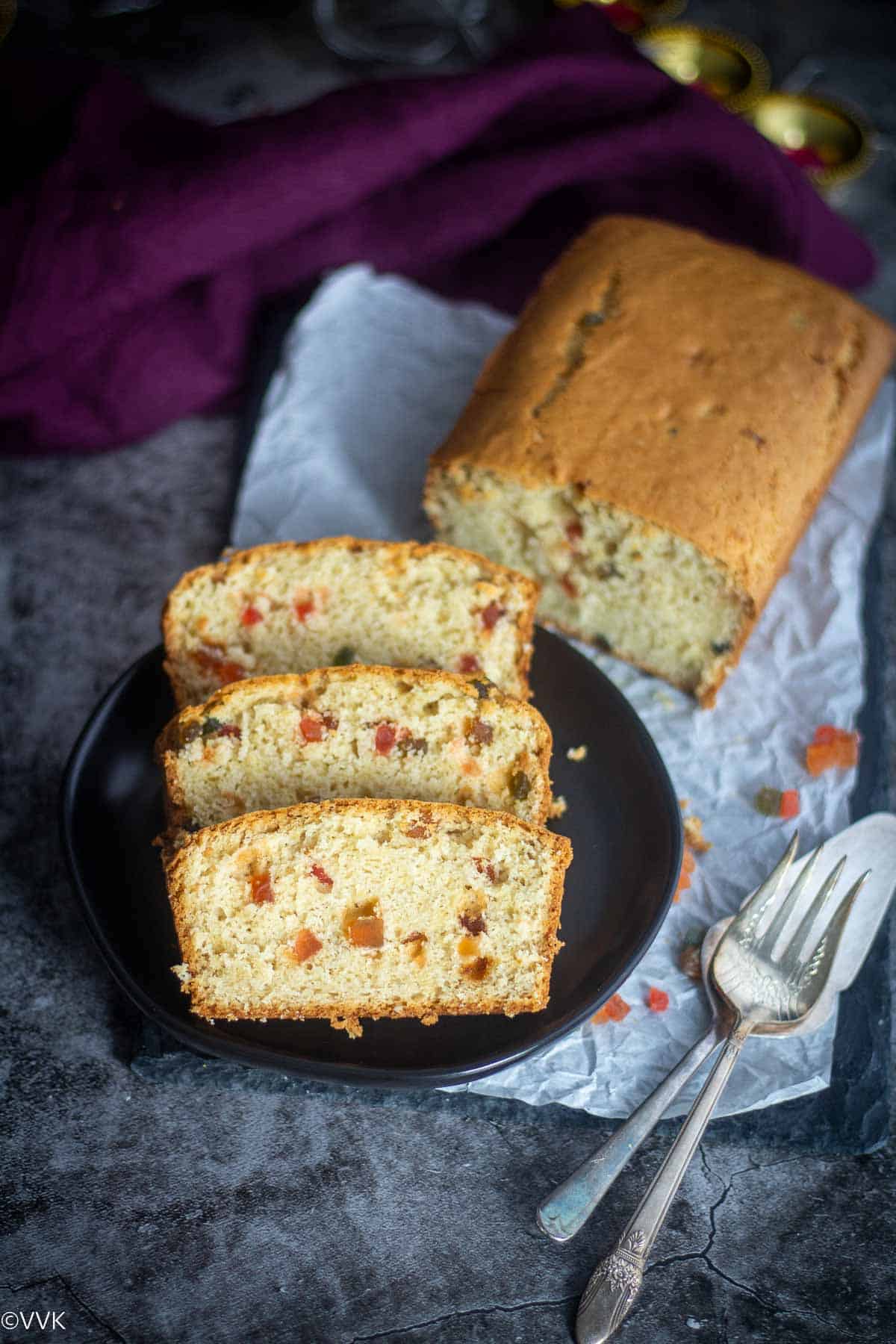 tutti frutti cake loaf with three cut slices placed in a black plate