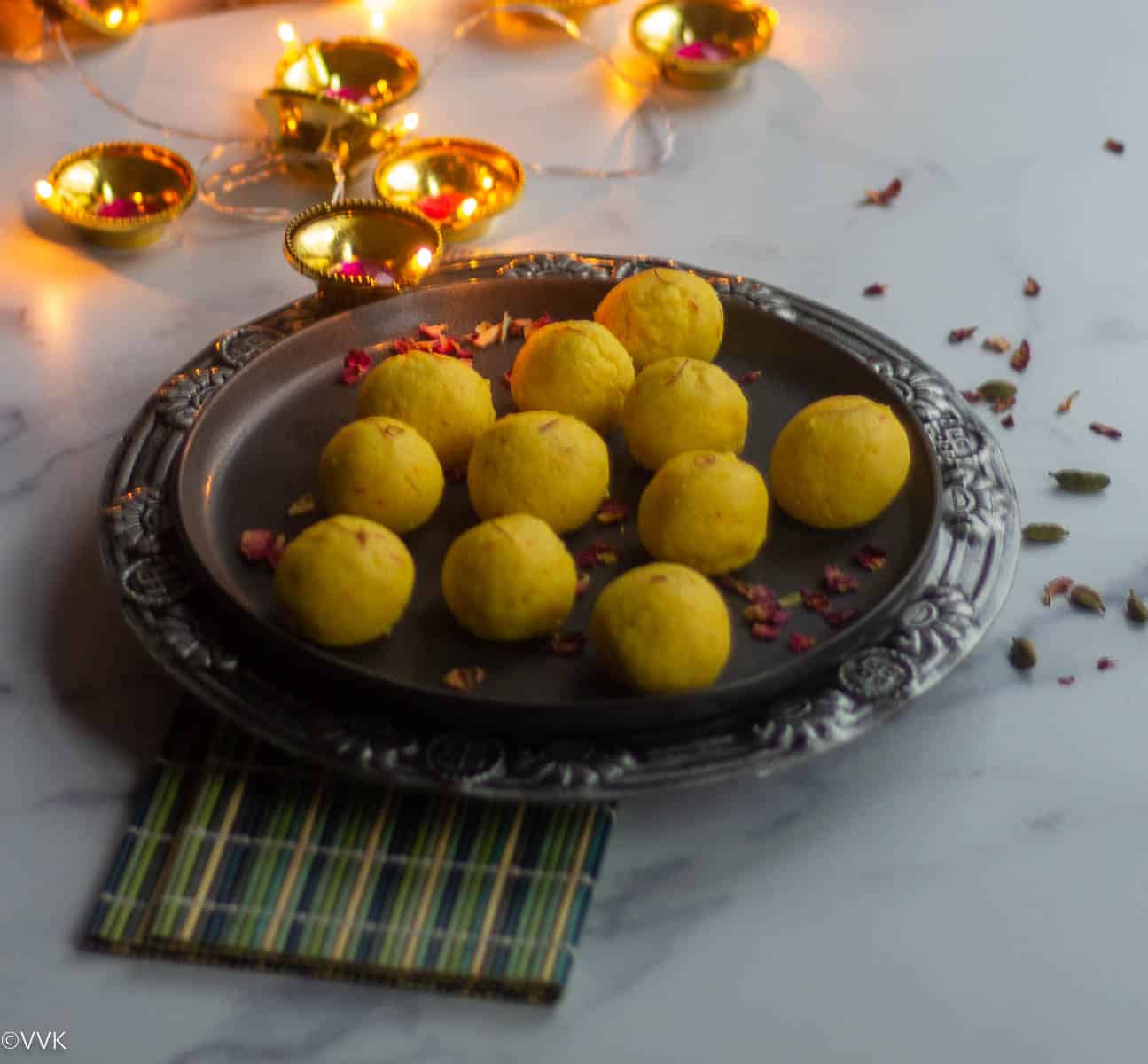 paneer ladoo served on ceramic plate placed on green mat with some lights on the background