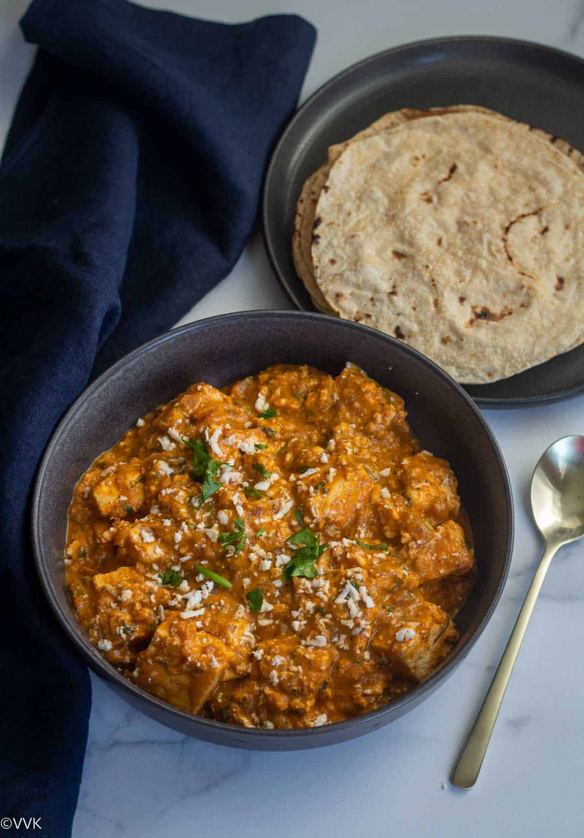 paneer lababdar curry with roti on the side with blue fabric and spoon on the side