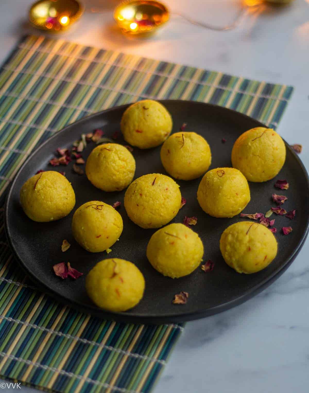 malai laddu served in ceramic plate garnished with rose petals placed on a green mat