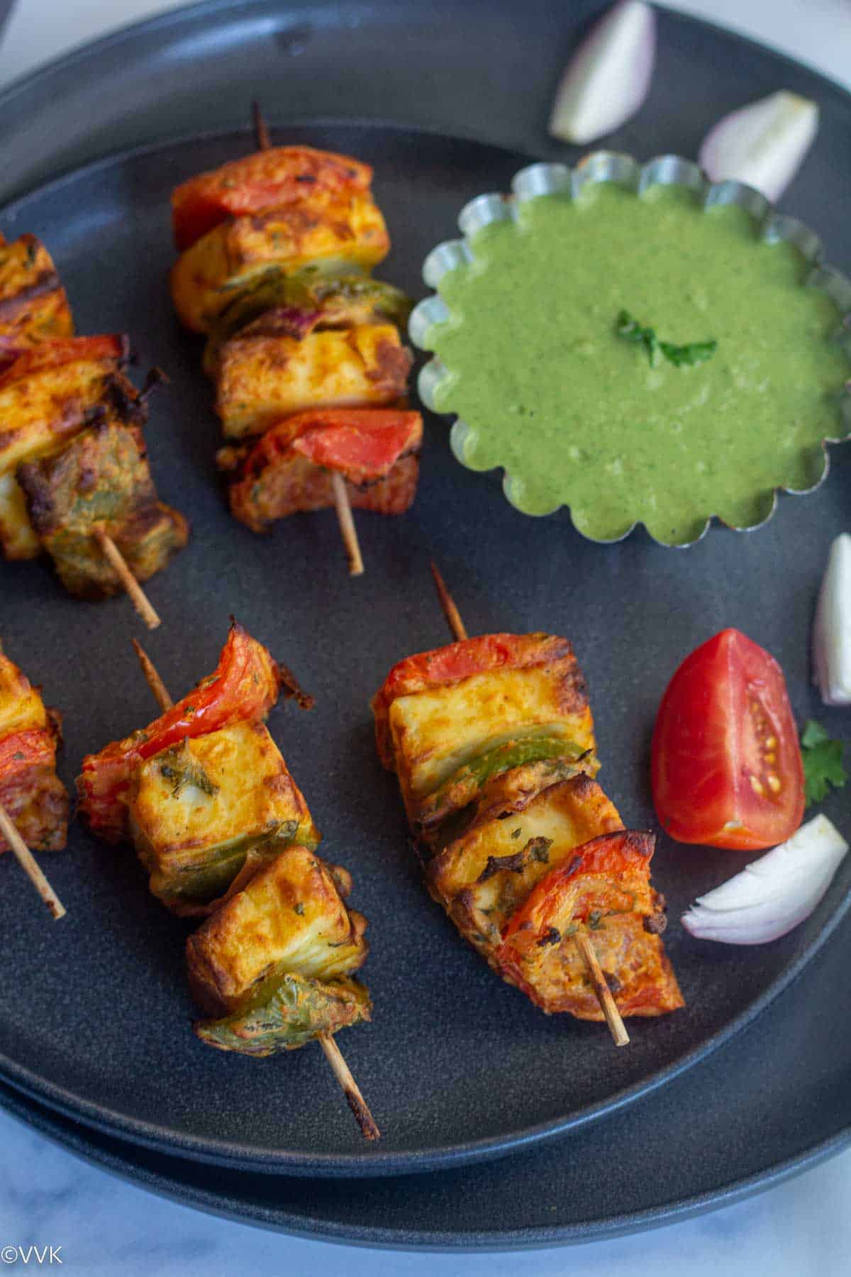 close up shot of tandoori paneer served in black plate with onions and tomatoes and green chutney