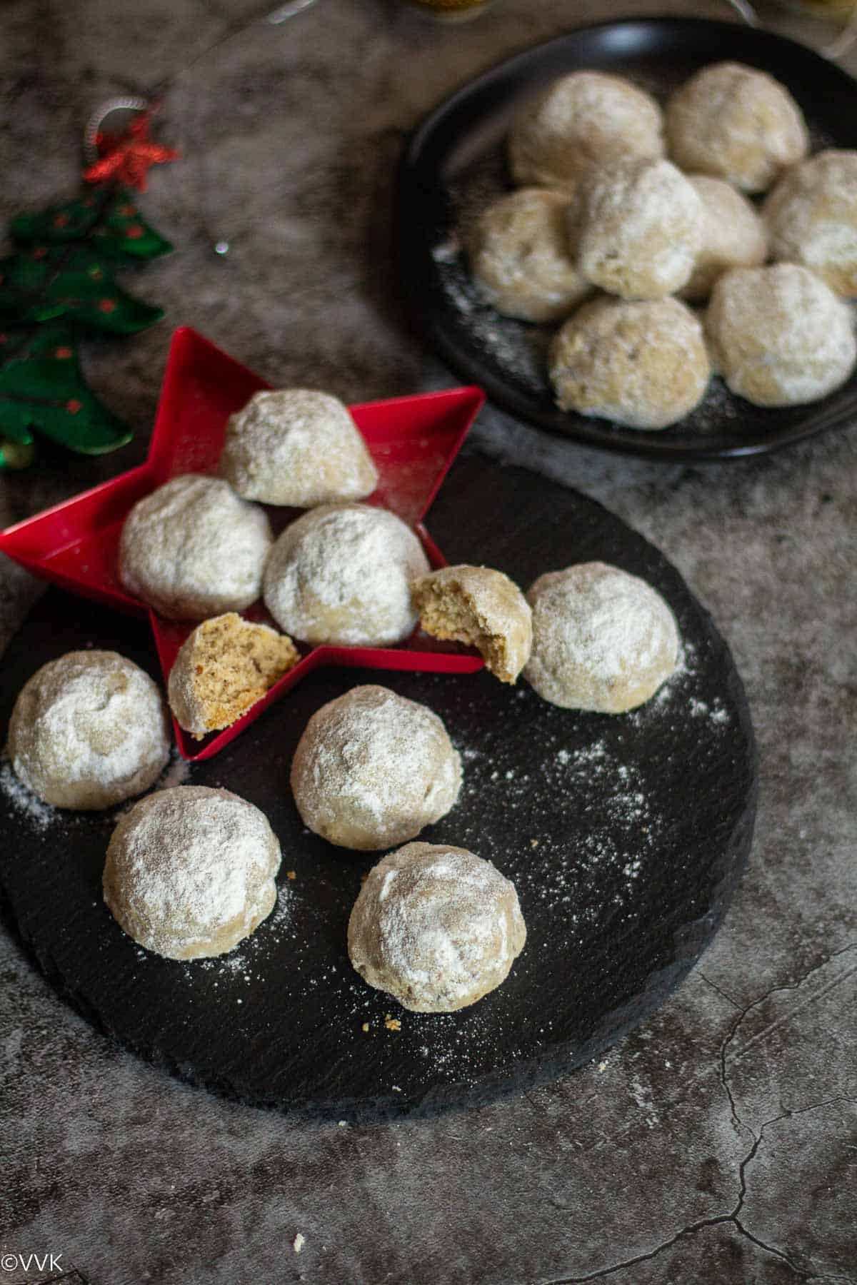 easy snowball cookies with walnuts and pecans placed on a black plate with one cookie cut into half