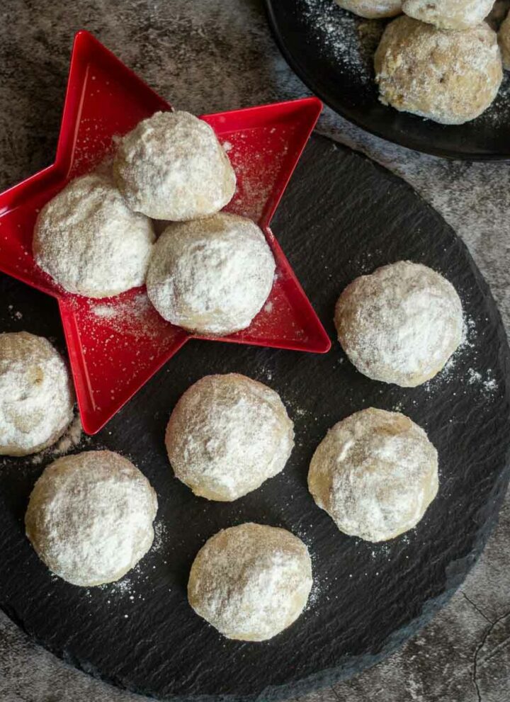 square image of snowball cookies placed on black board and on star plate