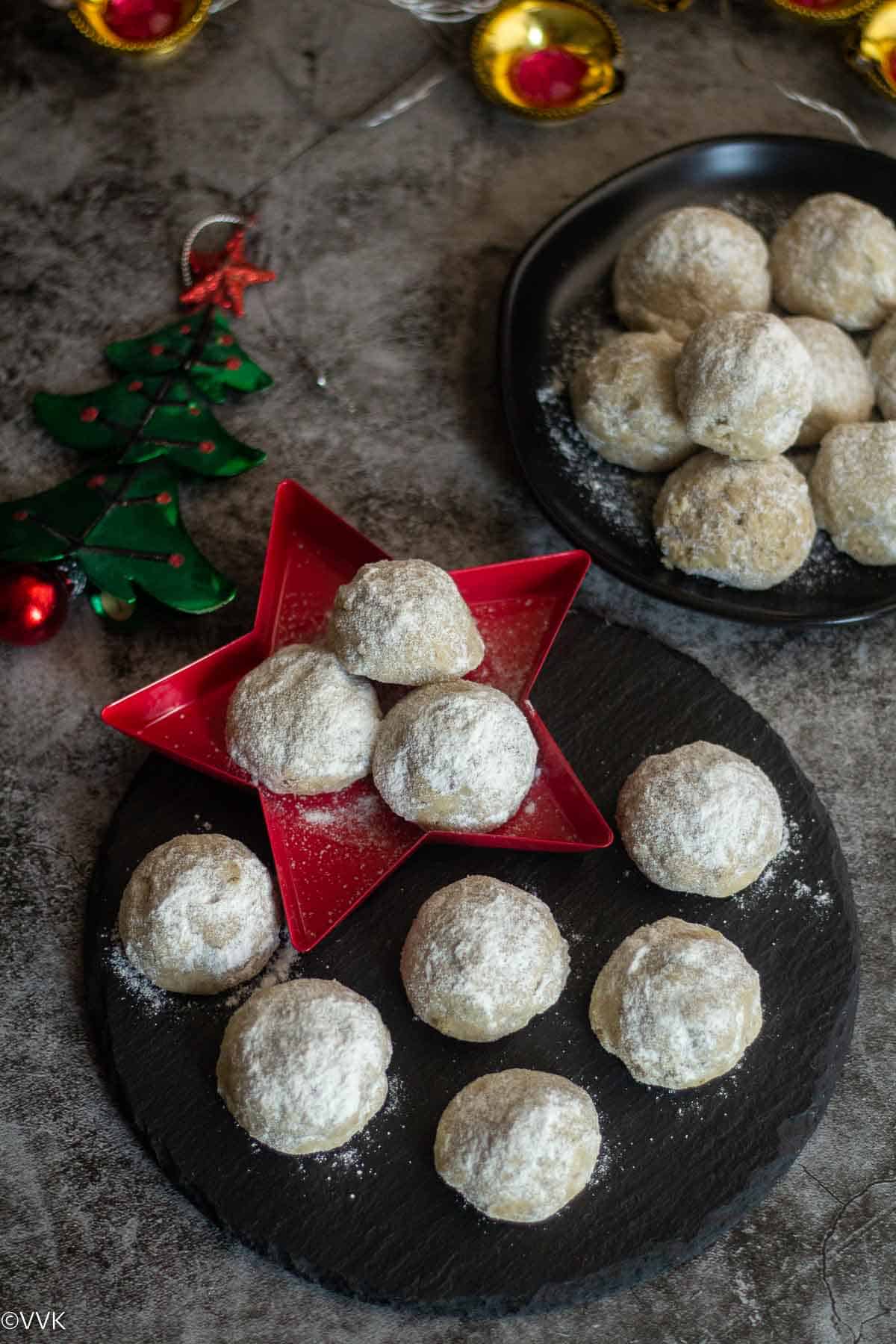 snowball cookies placed on blackplate and star plate with xmas tree on a side