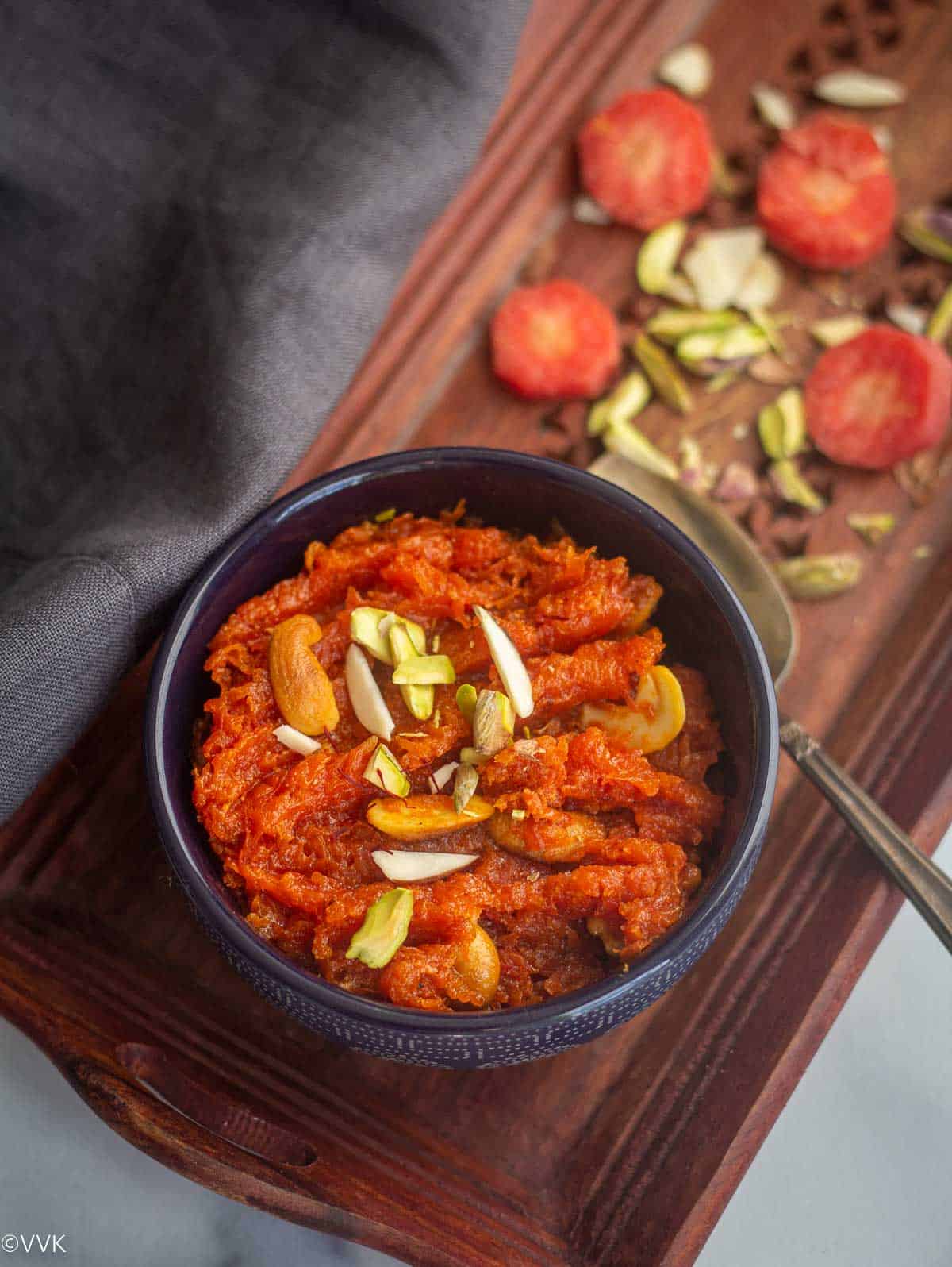 gajar ka halwa served in blue bowl with some nuts and carrots on the side on a wooden tray