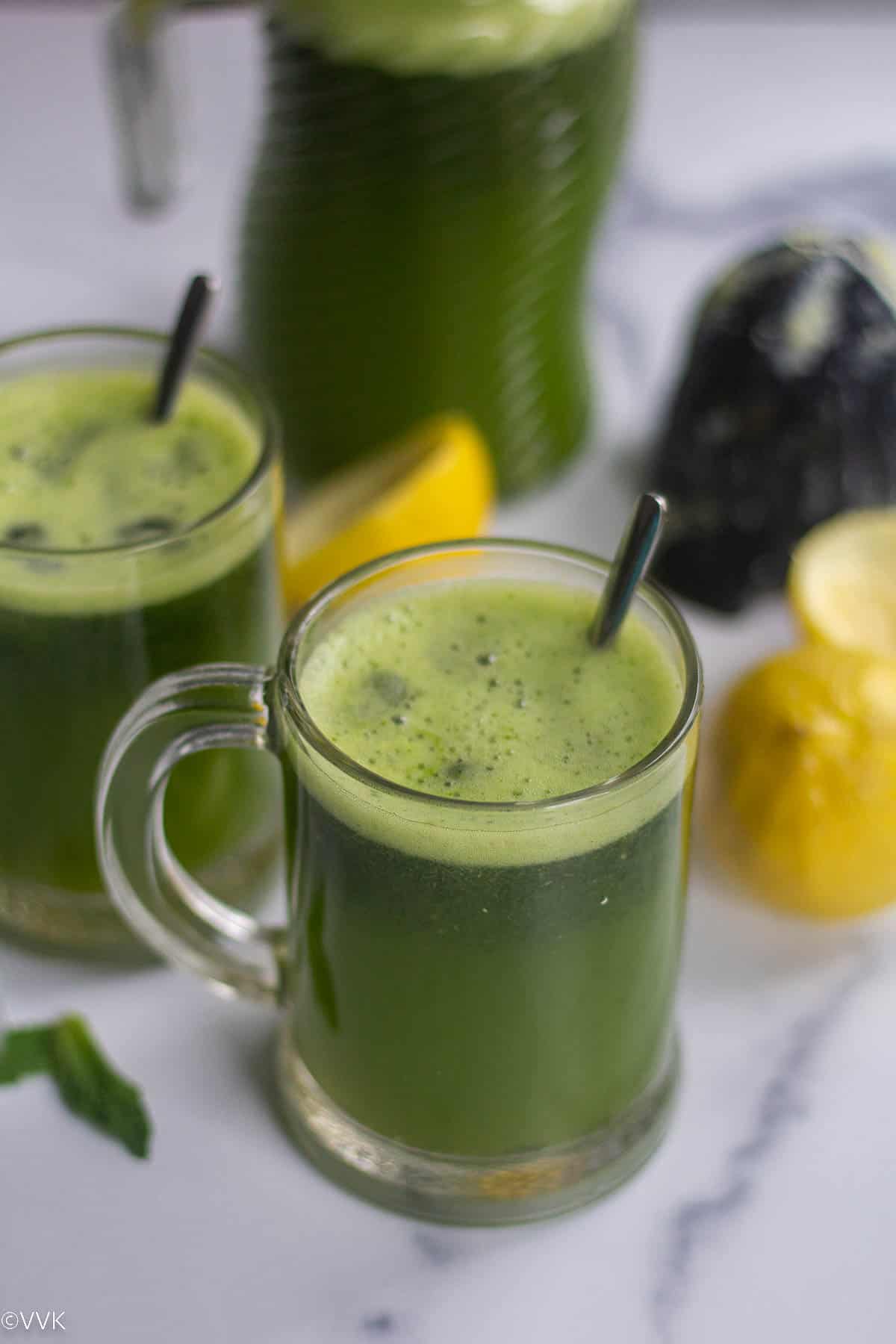 straight shot of limonana served in glass with spoon inside with squeezed lemons on the side