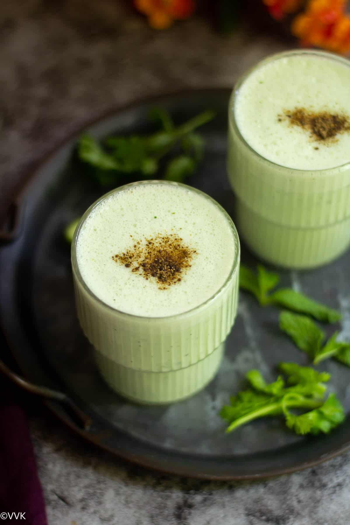 cucumber lassi served in two glasses with chaat masala sprinkled on top
