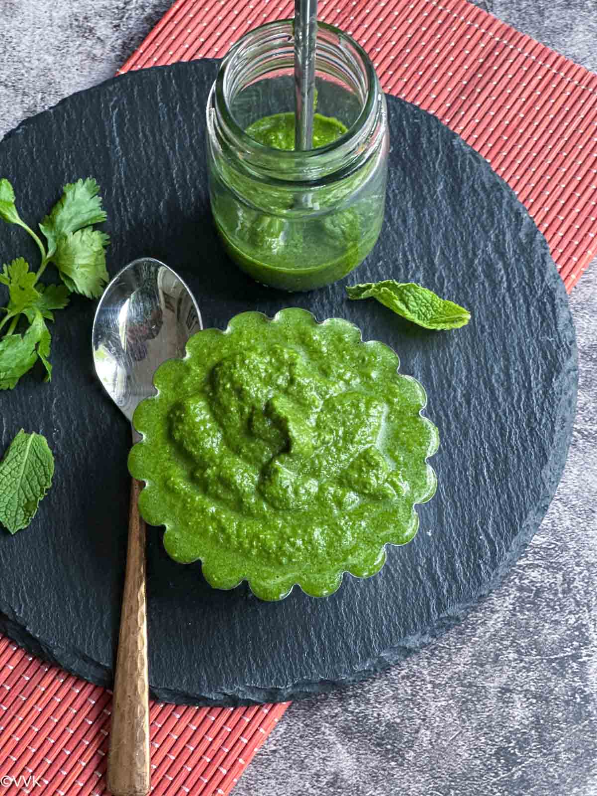 close up shot of green chutney served in bowl and a small glass jar