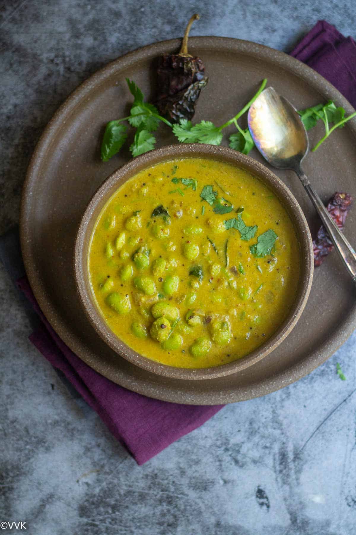 overhead shot of edamame huli saaru served in round ceramic bowl with cilantro and red chili on the side