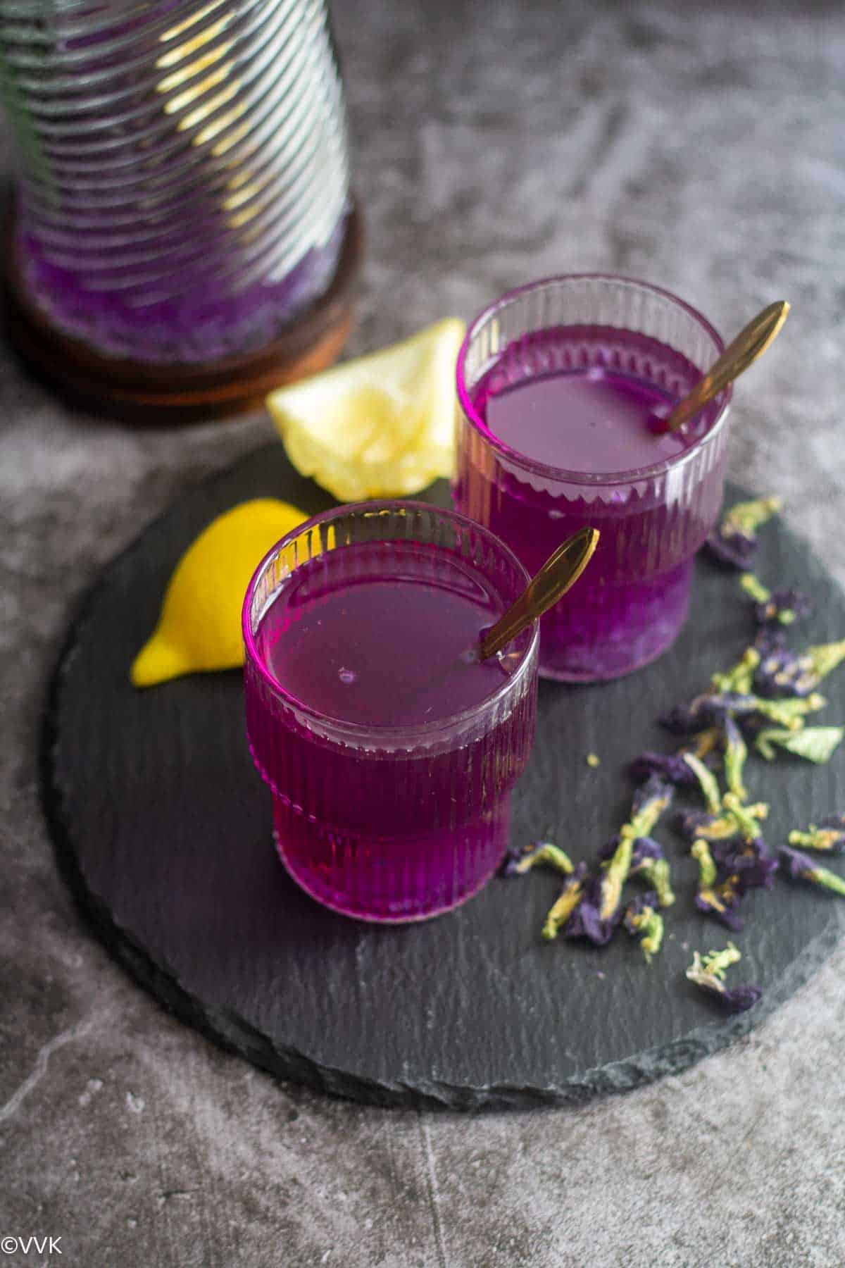 overhead slanting shot of butterfly pea lemonade with dried flowers and lemon on the side