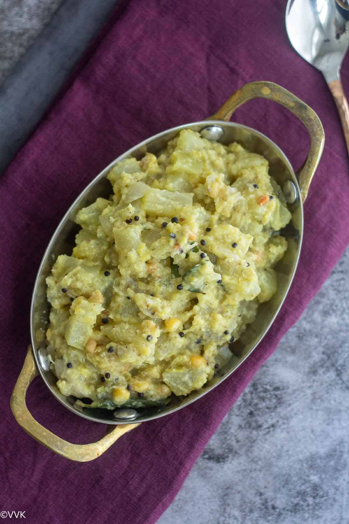 a slightly close up shot of raw papaya kootu served in oval vessel placed on purple towel