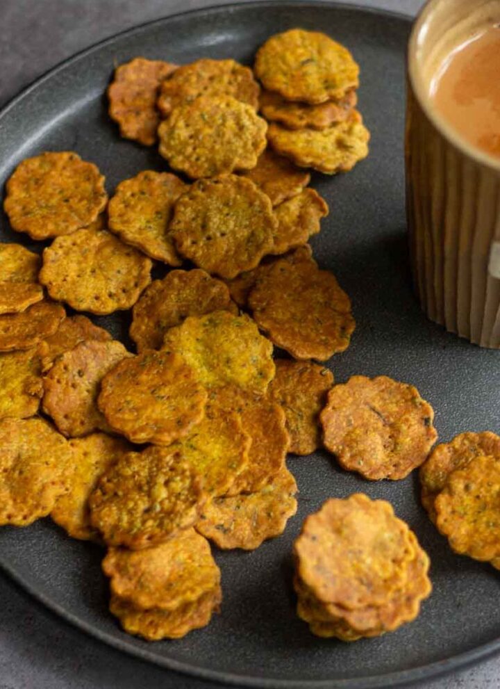 square image of baked methi mathri served with tea