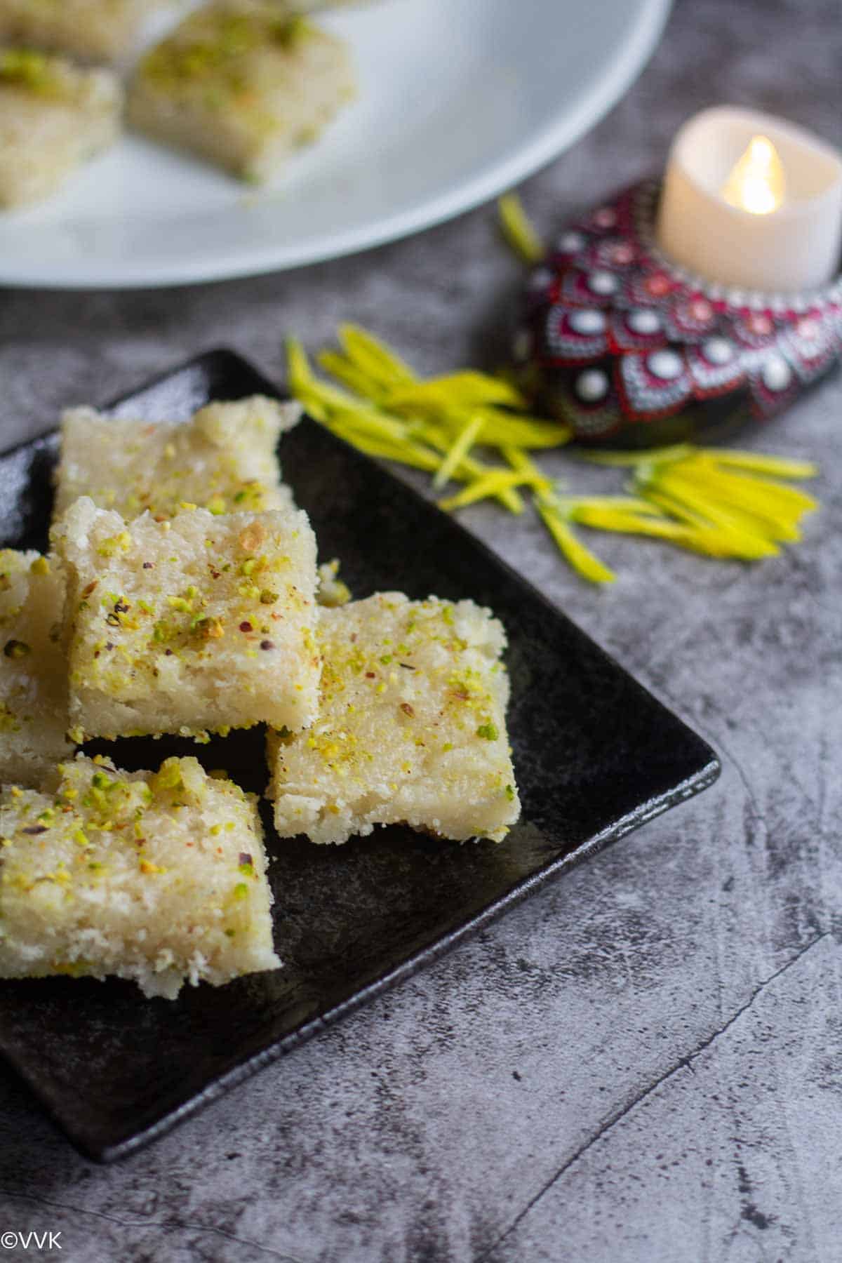 slanting shot of coconut burgi placed on black plate