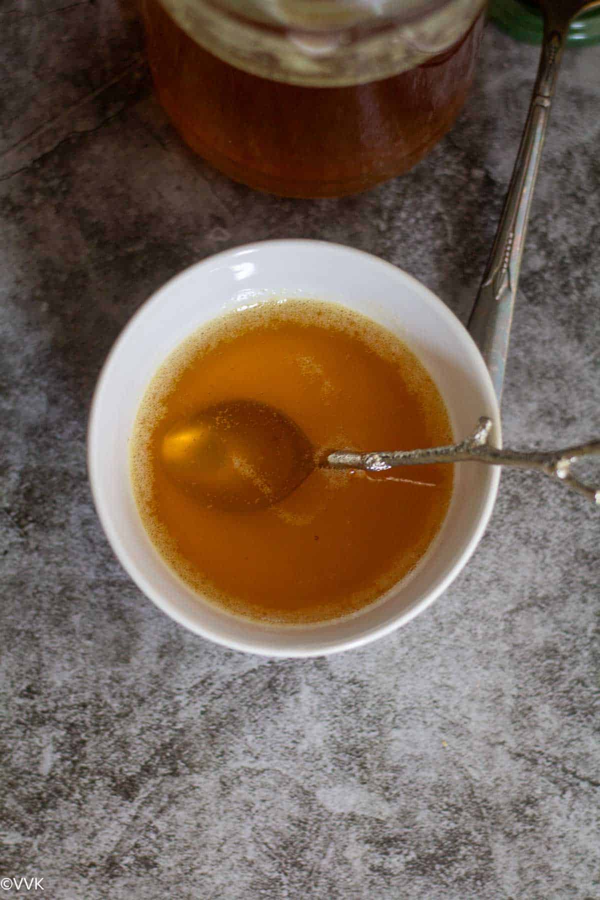 clear ghee liquid aka clarified butter in white bowl with spoon inside