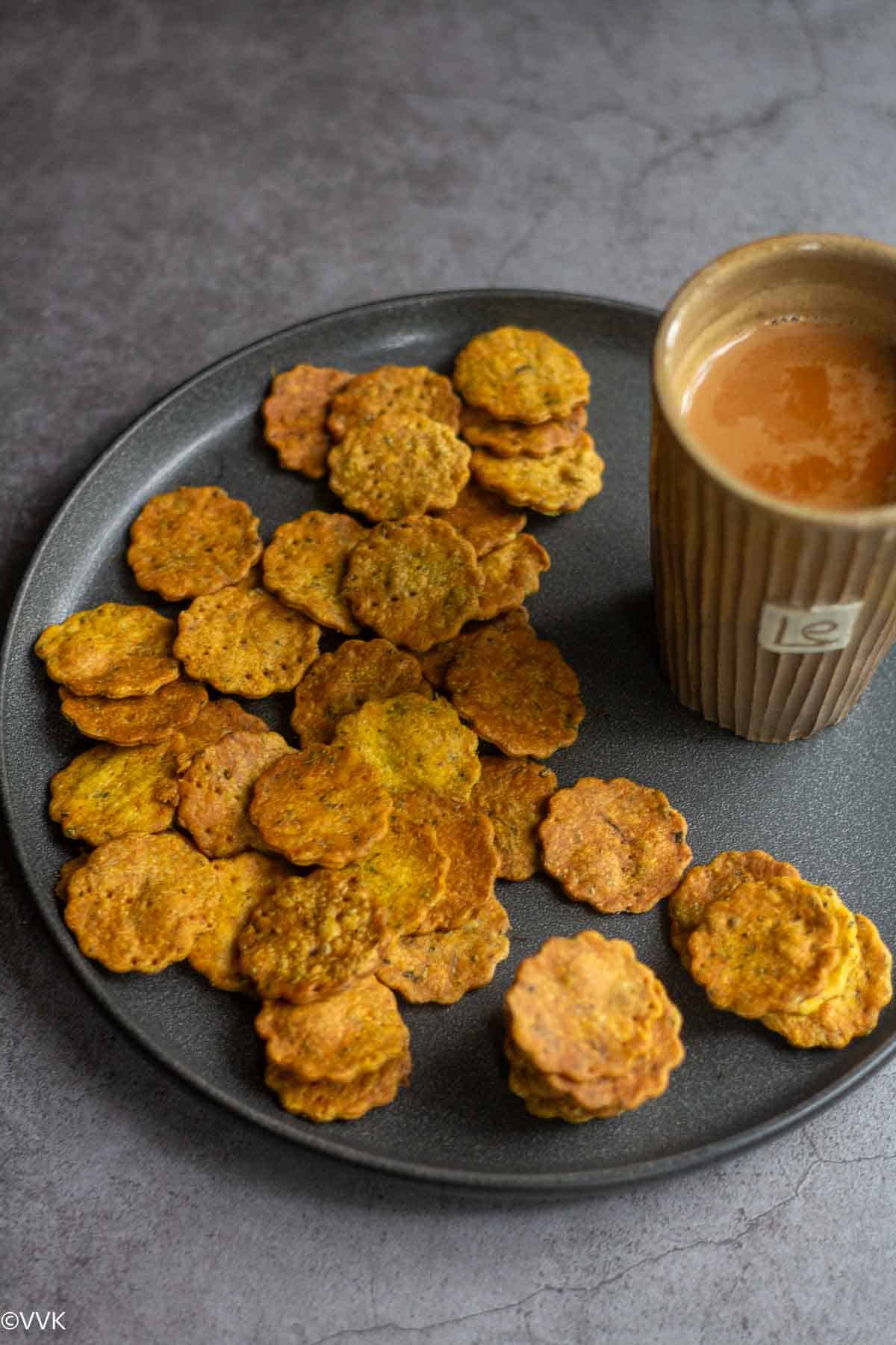 Baked mathri loaded in a plate with tea on the side