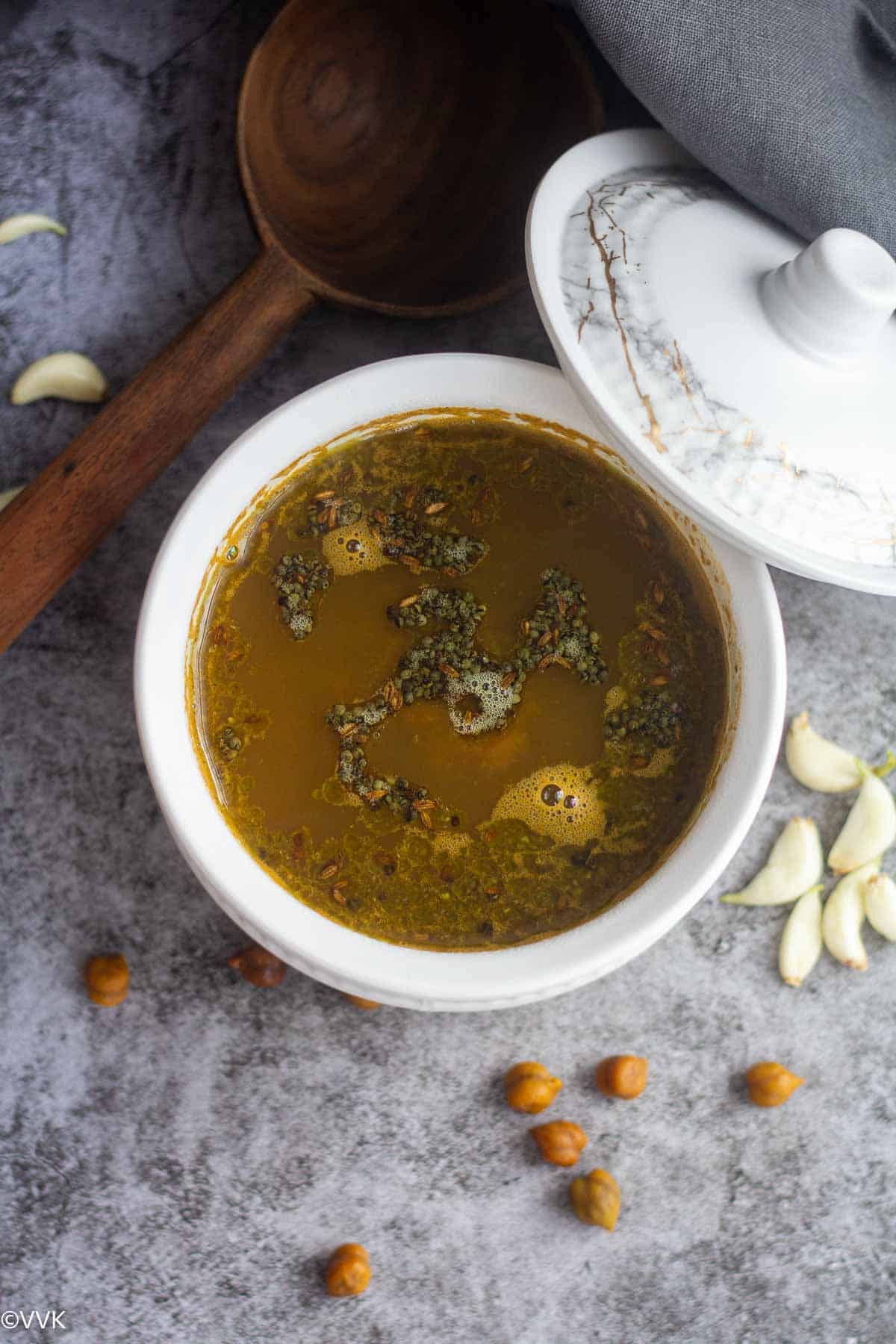 overhead shot of kadala rasam with the tempering on top with dried chickpeas and garlic on the side