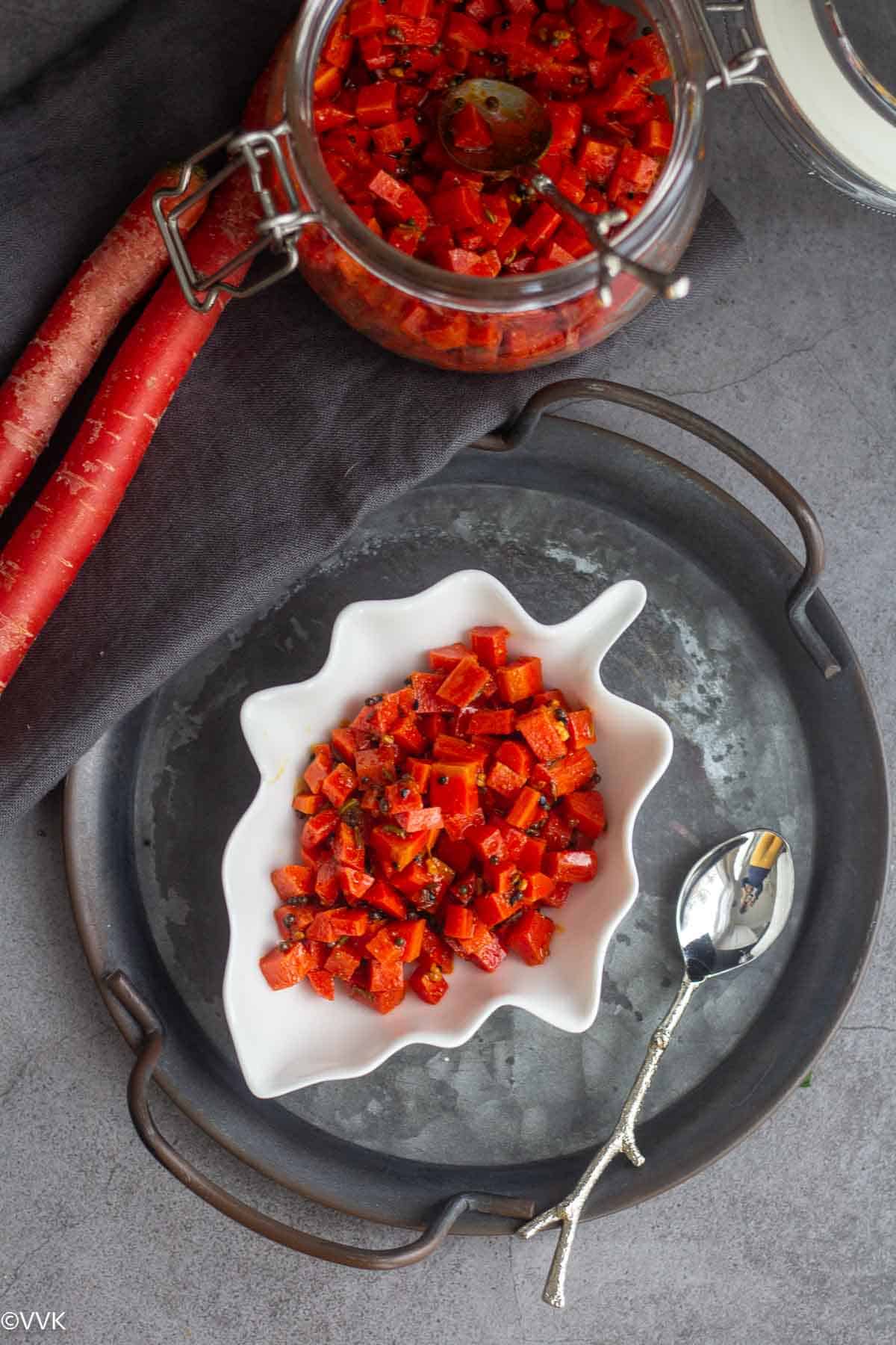 overhead shot of carrot pickle placed on a white leaf bowl with a jar or carrot pickles on the side
