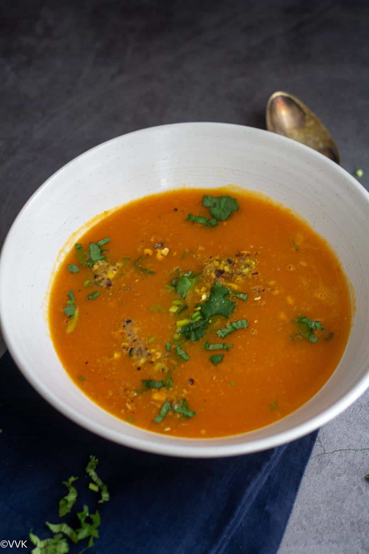 carrot soup served in white bowl with the spoon on the side