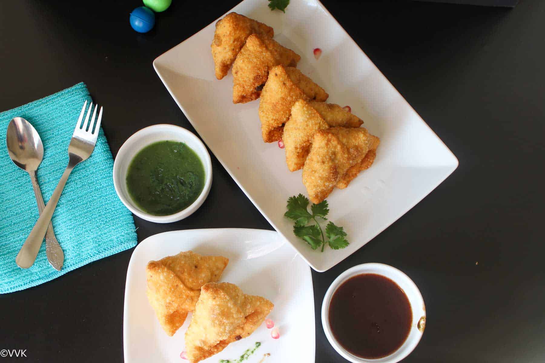 samosa stacked in two plates with chutneys on side