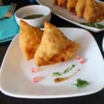 square image of two samosa placed on white plate