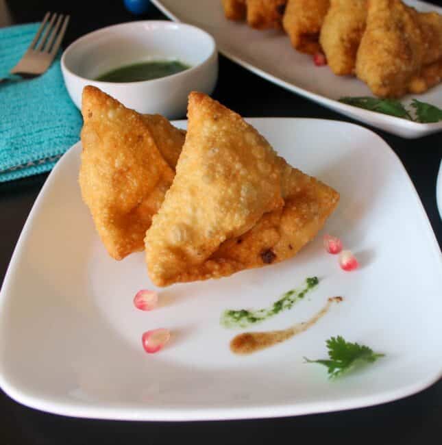 square image of two samosa placed on white plate