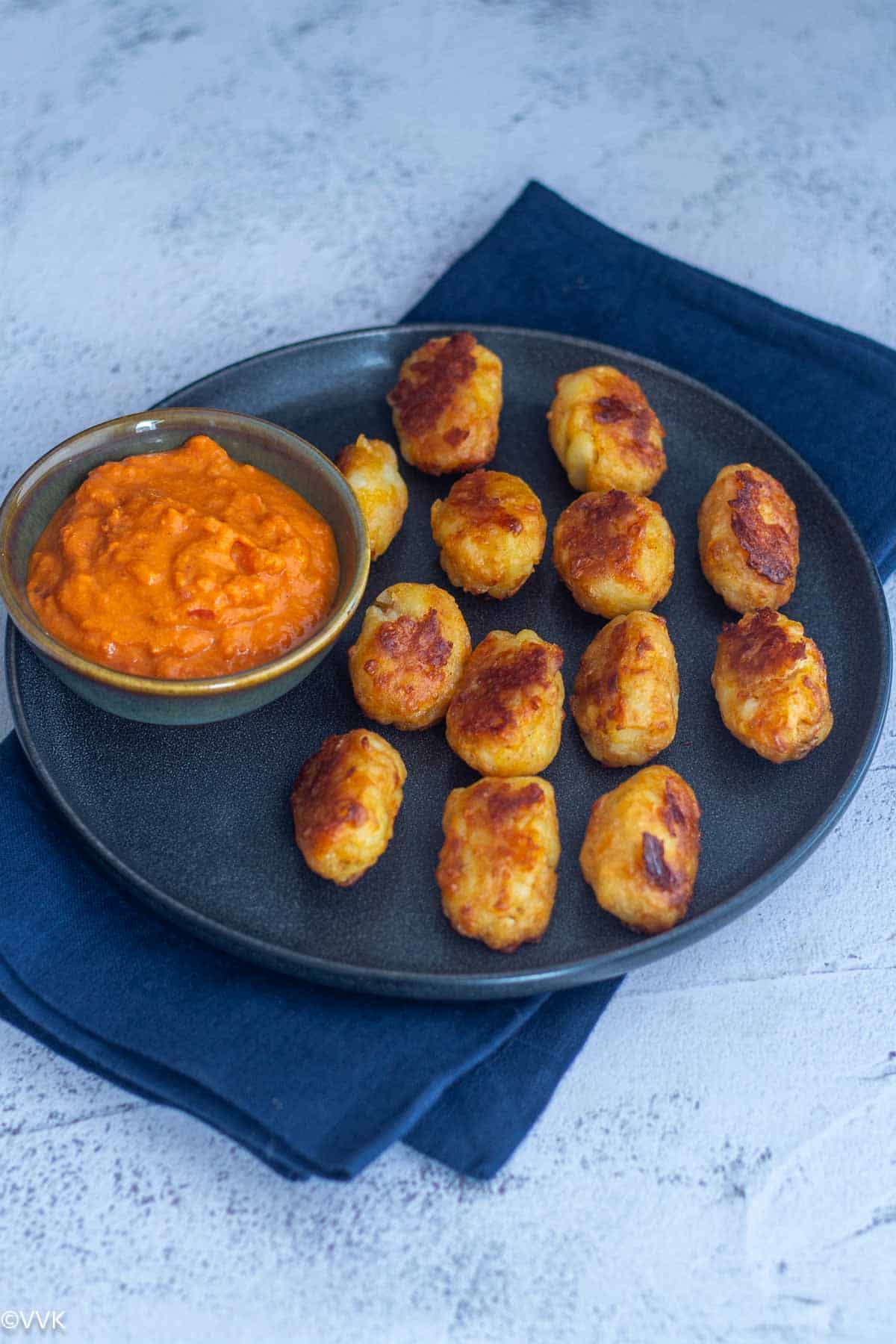 slanting shot of tater tots with sauce in a bowl placed on a ceramic plate