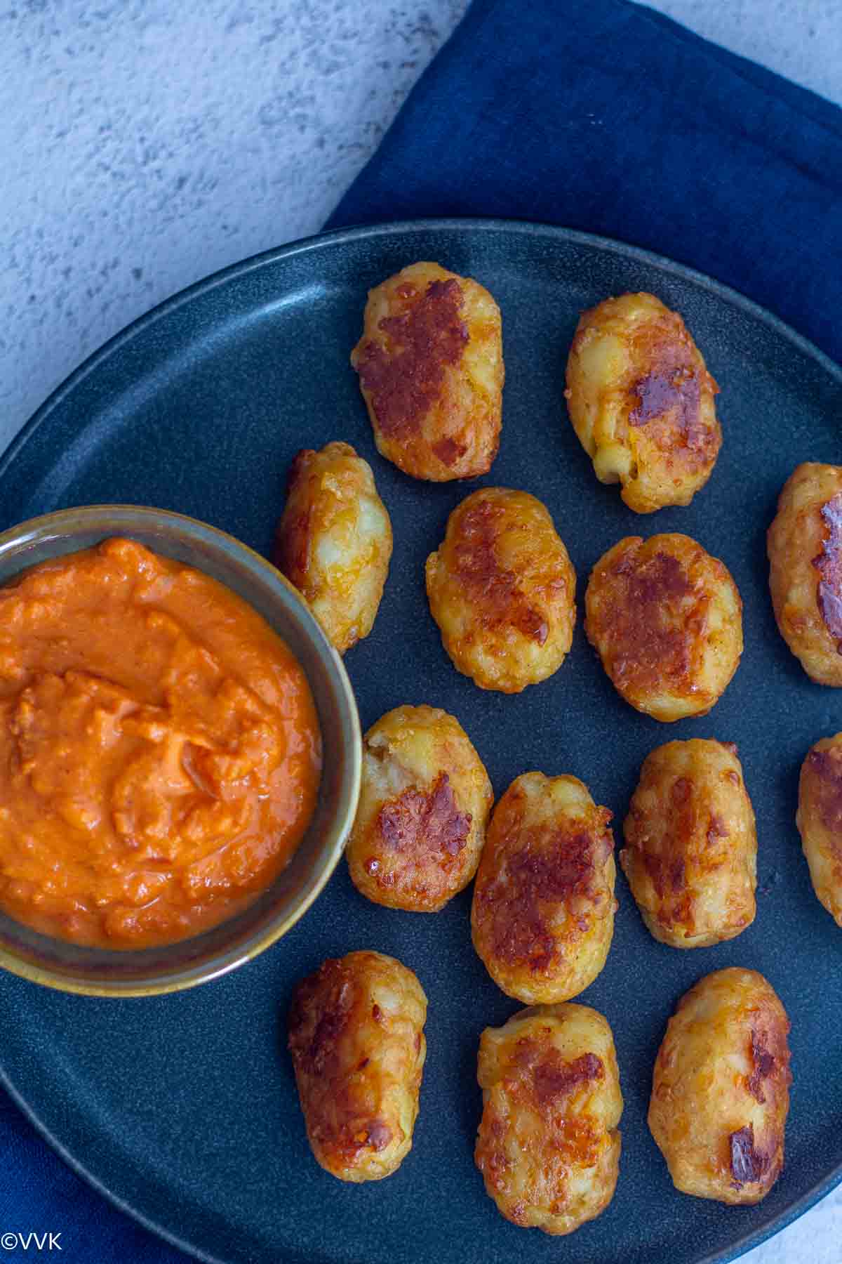 close up shot of baked tater tots served in a plate with marinara in a cup