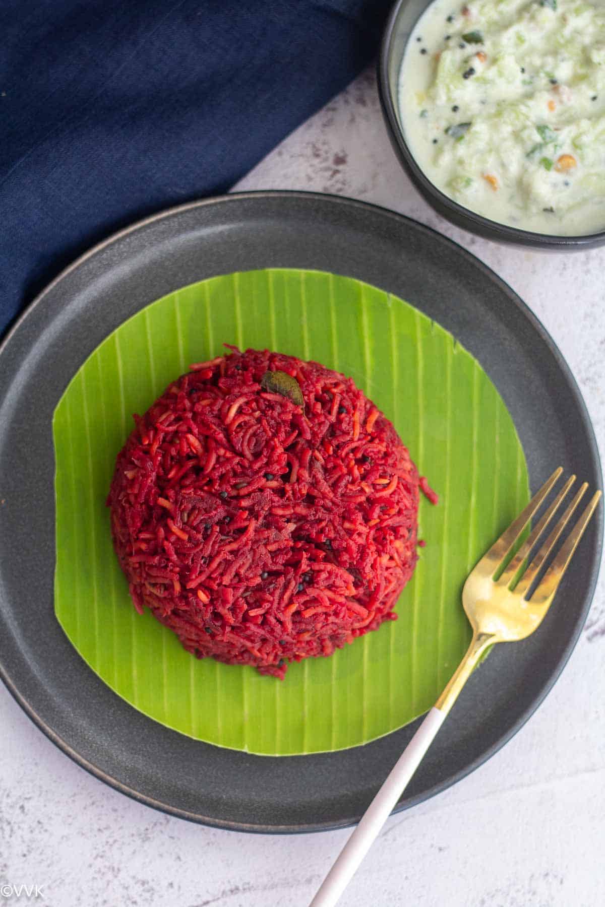 overhead shot of beetroot rice served in plate lined with banana leaf and cucumber raita