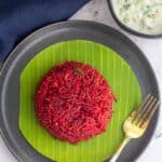 square image of beets pulao served in banana leaf placed on a plate