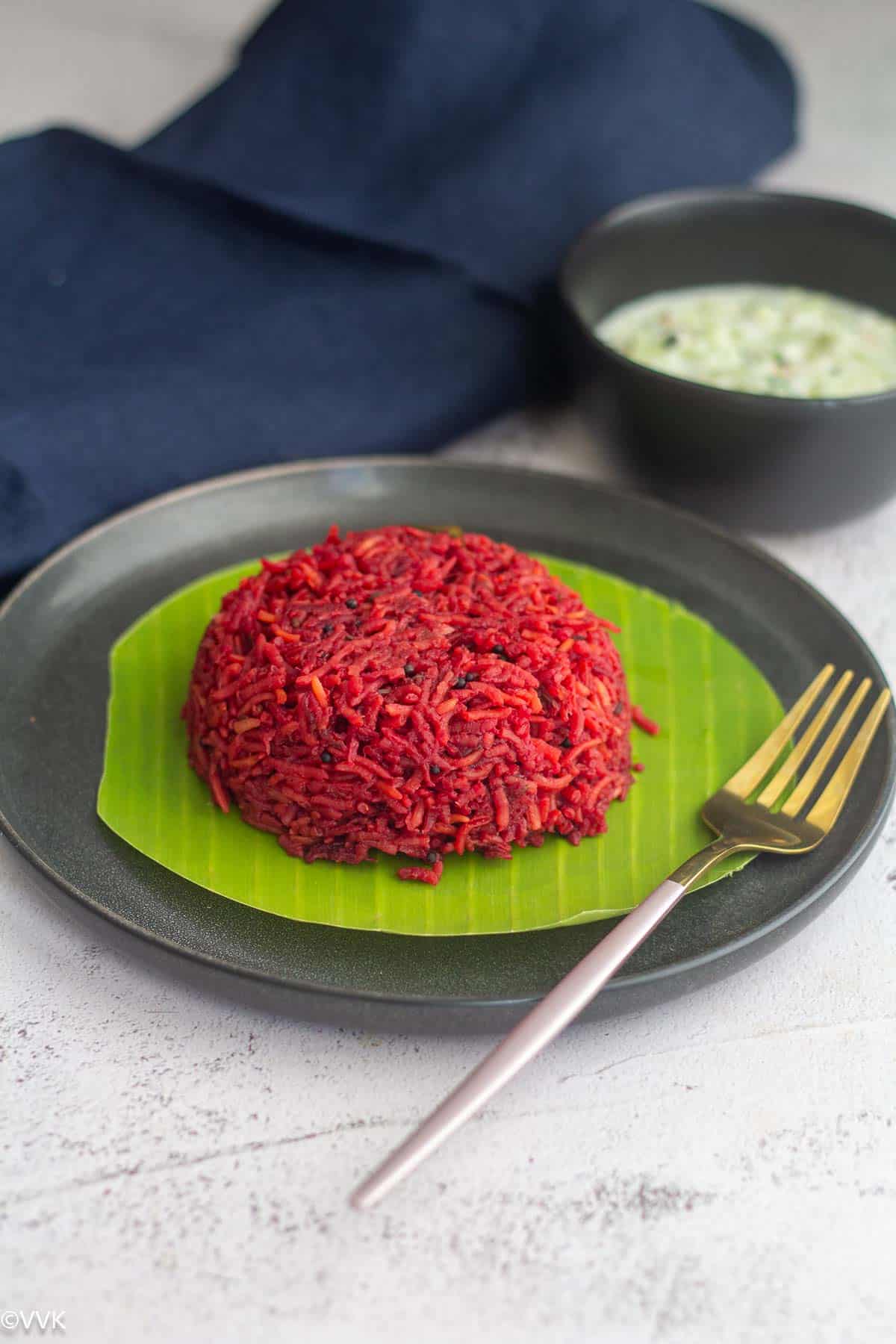 slanting shot of beetroot rice placed on a plate lined with banana leaf with a fork on the side