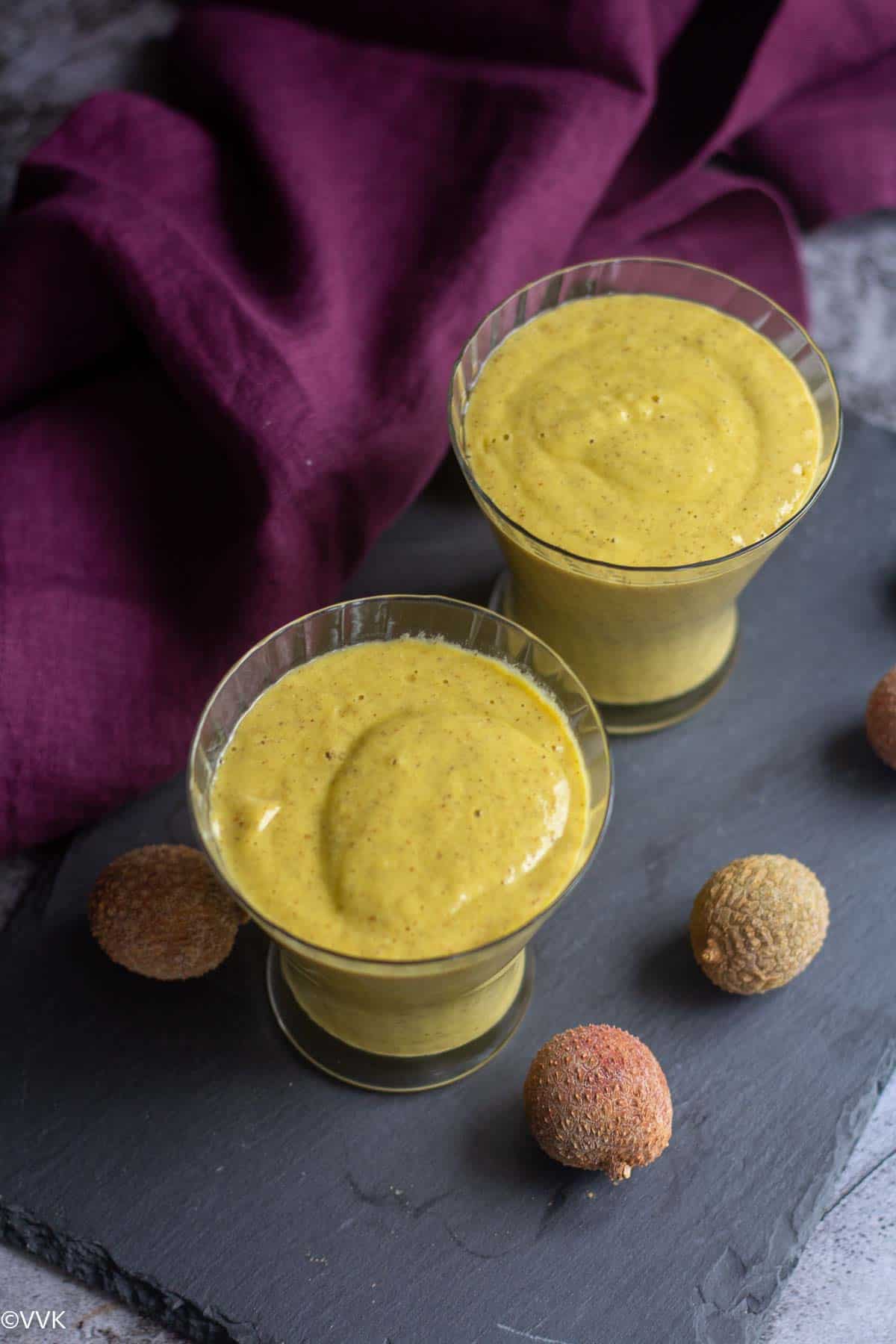 slanting shot of vegan tropical smoothie served in two glasses with lychee on the side