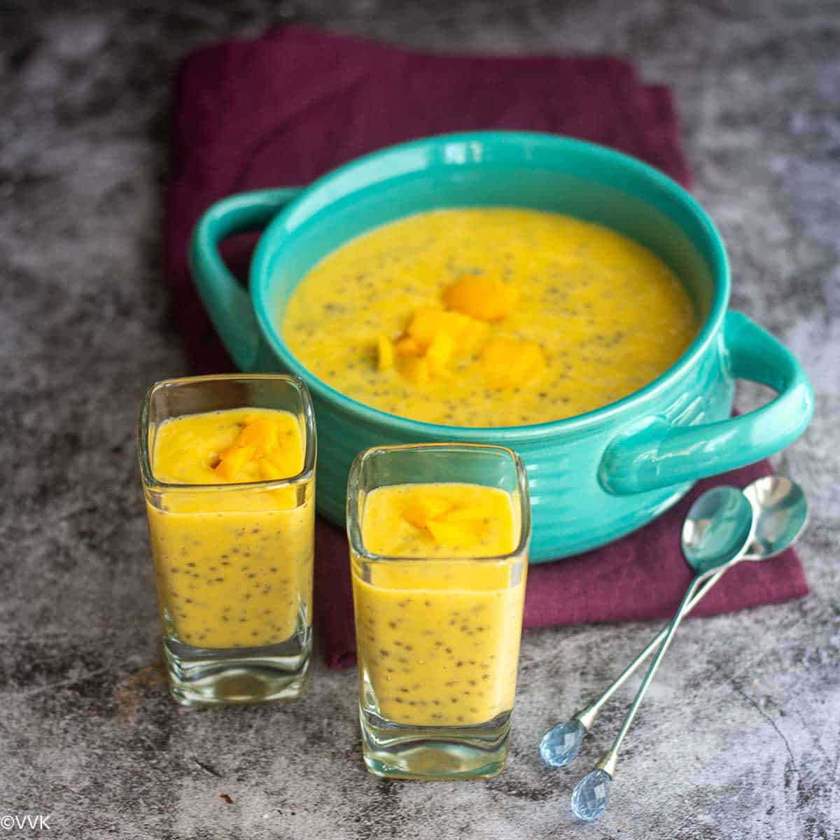 slanting shot of mango chia pudding served in teal bowl and two single serving glasses