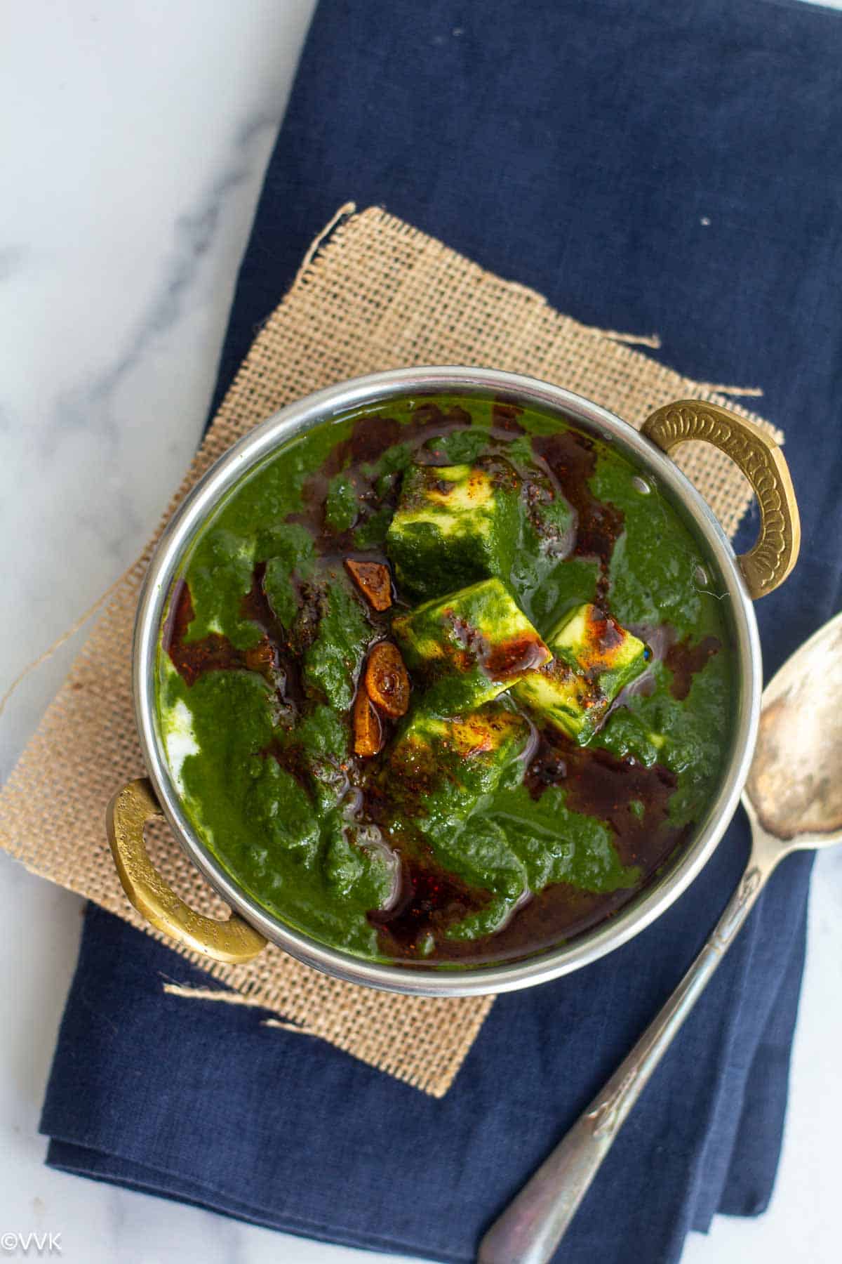 overhead shot of palak paneer served in kadai bowl placed on jute fabric