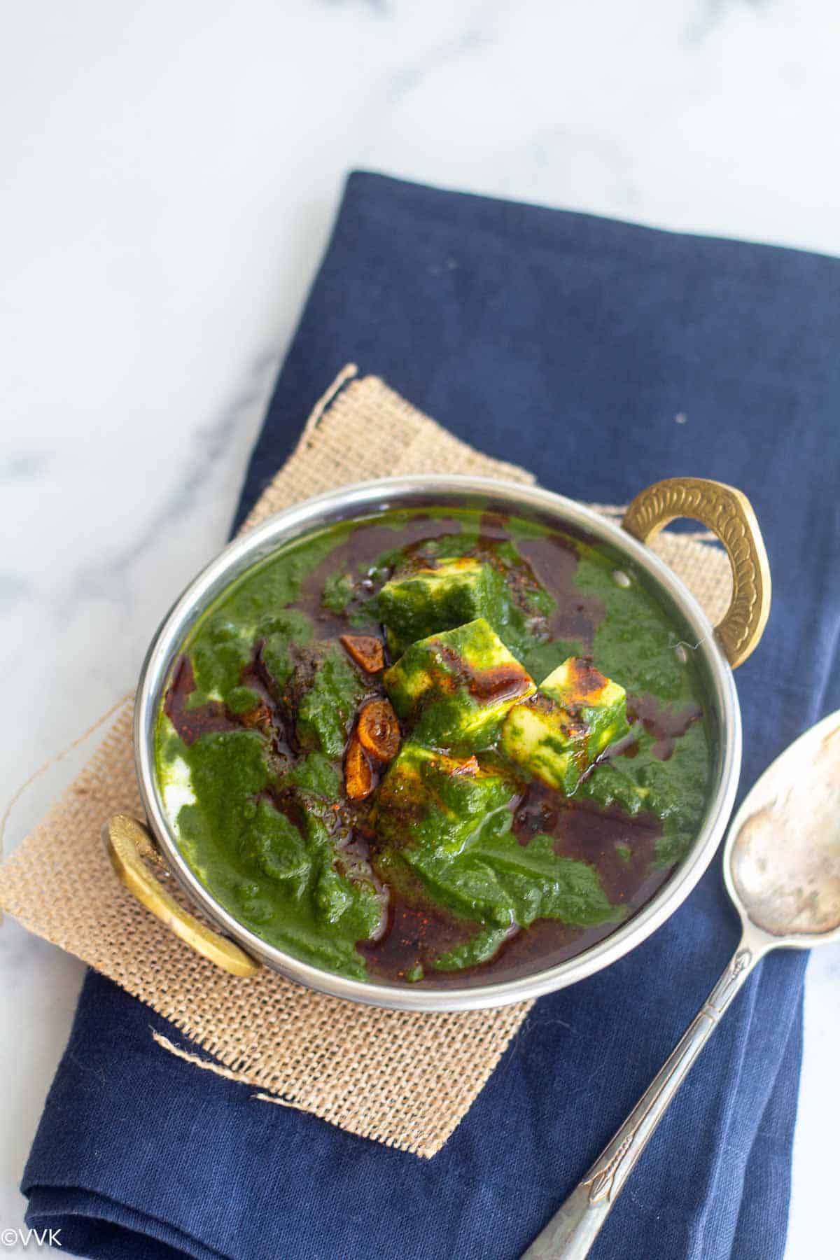slanting shot of palak paneer with chili powder tempering on top with spoon on the side