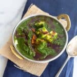 square image of palak paneer served in kadai bowl placed on jute fabric