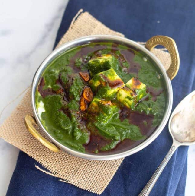 square image of palak paneer served in kadai bowl placed on jute fabric