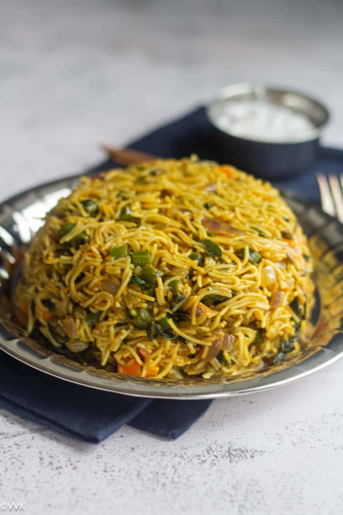 close up shot of semiya biryani served on a steel plate with raita on the side