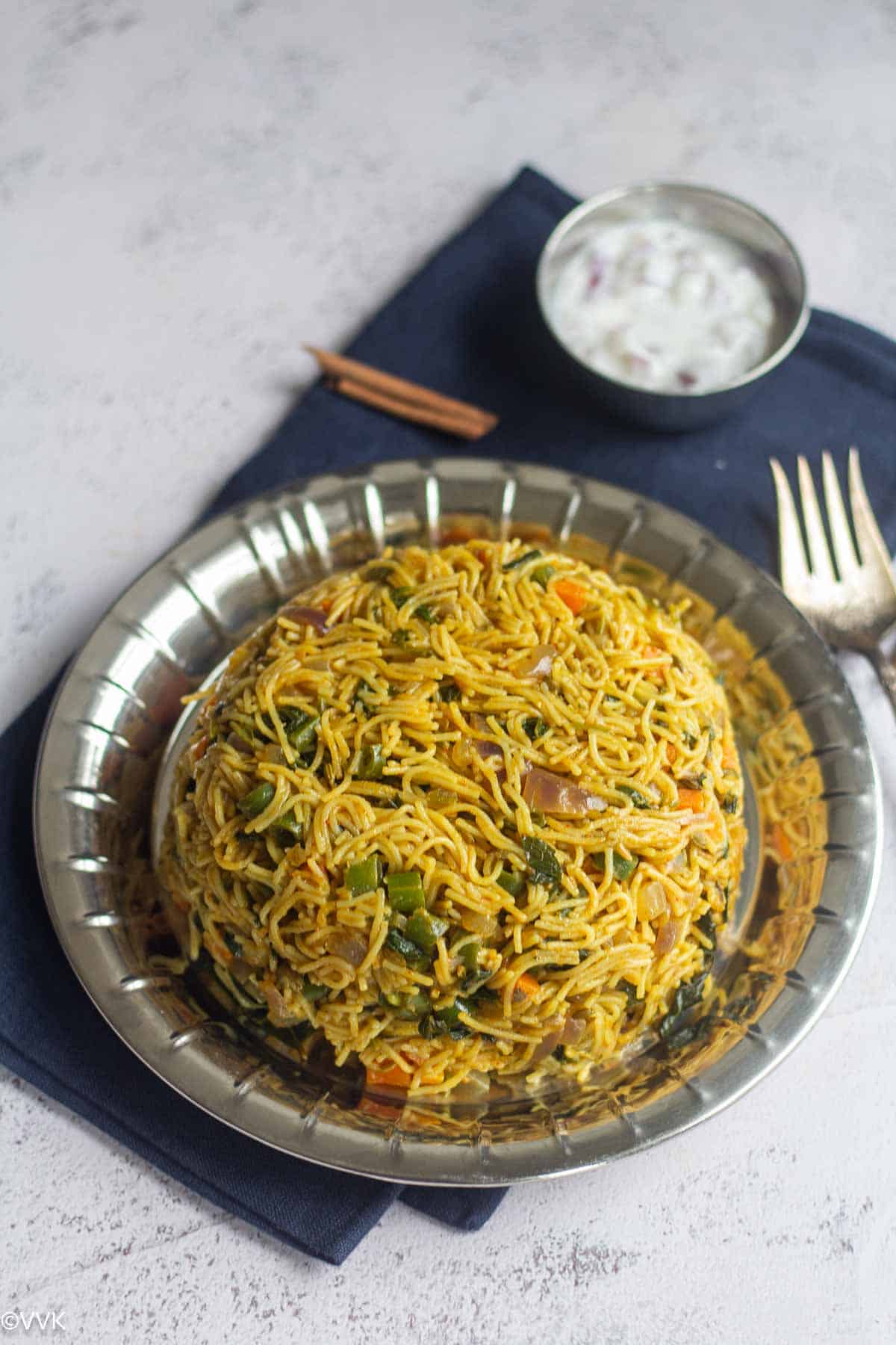a full view of semiya pulao served in stainless steel plate and with raita placed on blue napkin