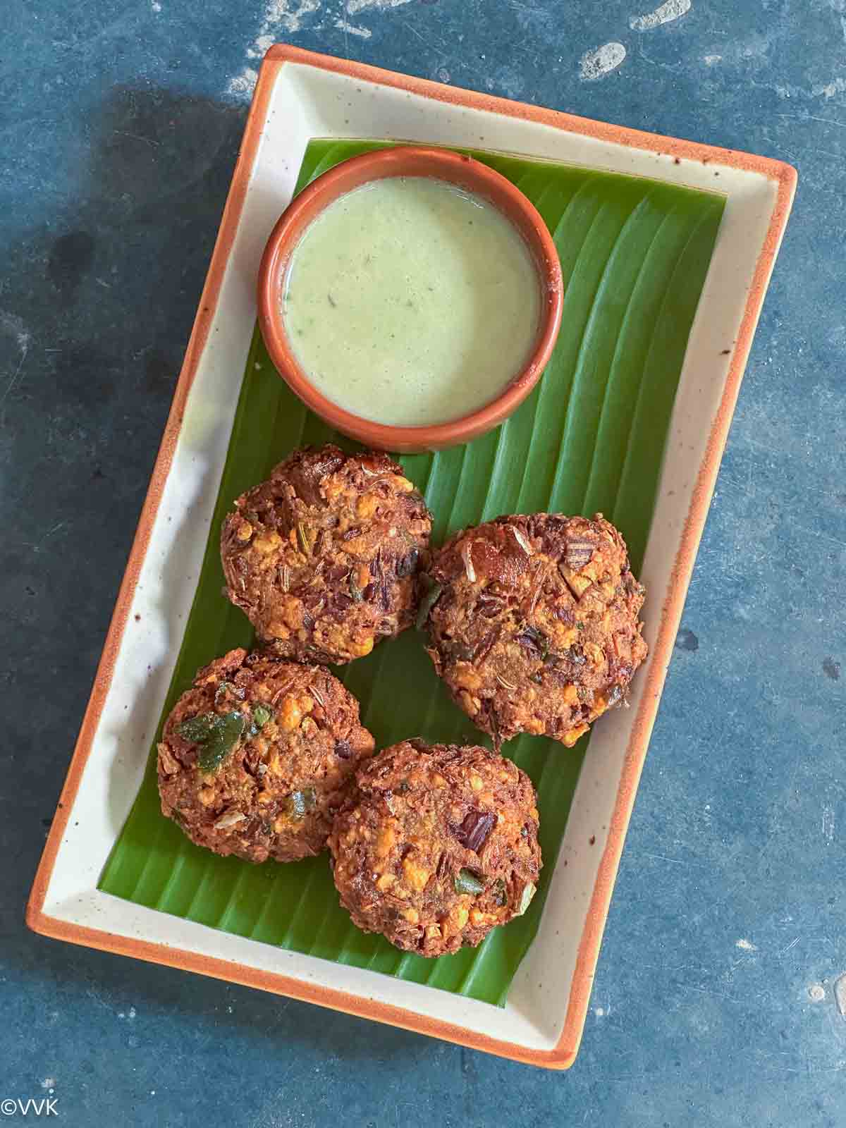 overhead shot of banana blossom fritters served with chutney in ceramic plate lined with banana leaf