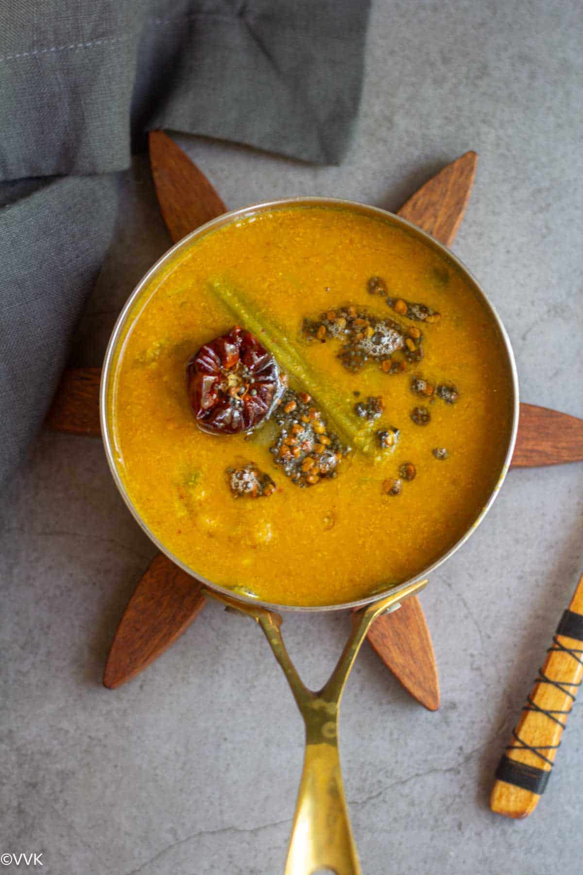 overhead shot of drumstick sambar with fresh coconut masala served in a copperware