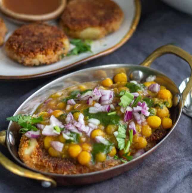 square image of white peas curry and aloo tikki served in copperware