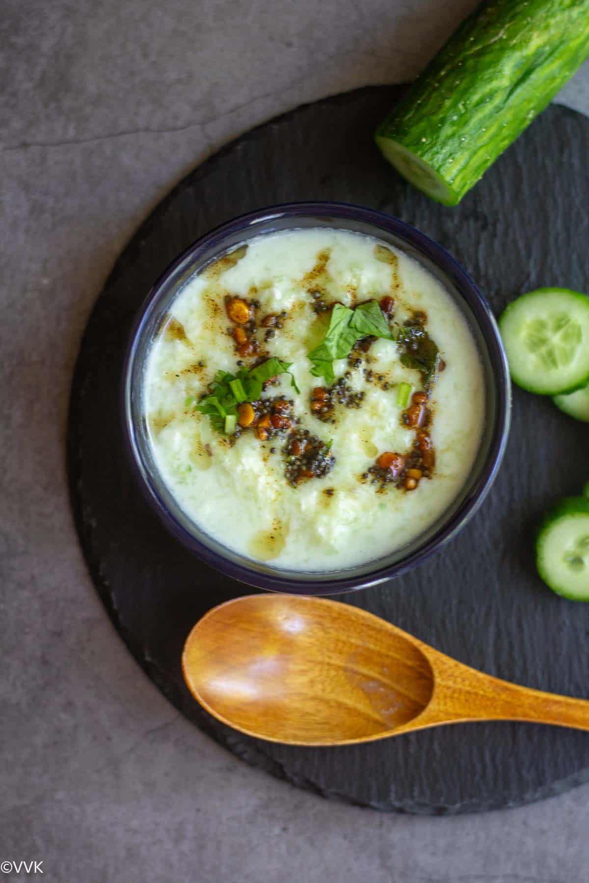 overhead shot of cucumber raita with tempering on top placed on black slate