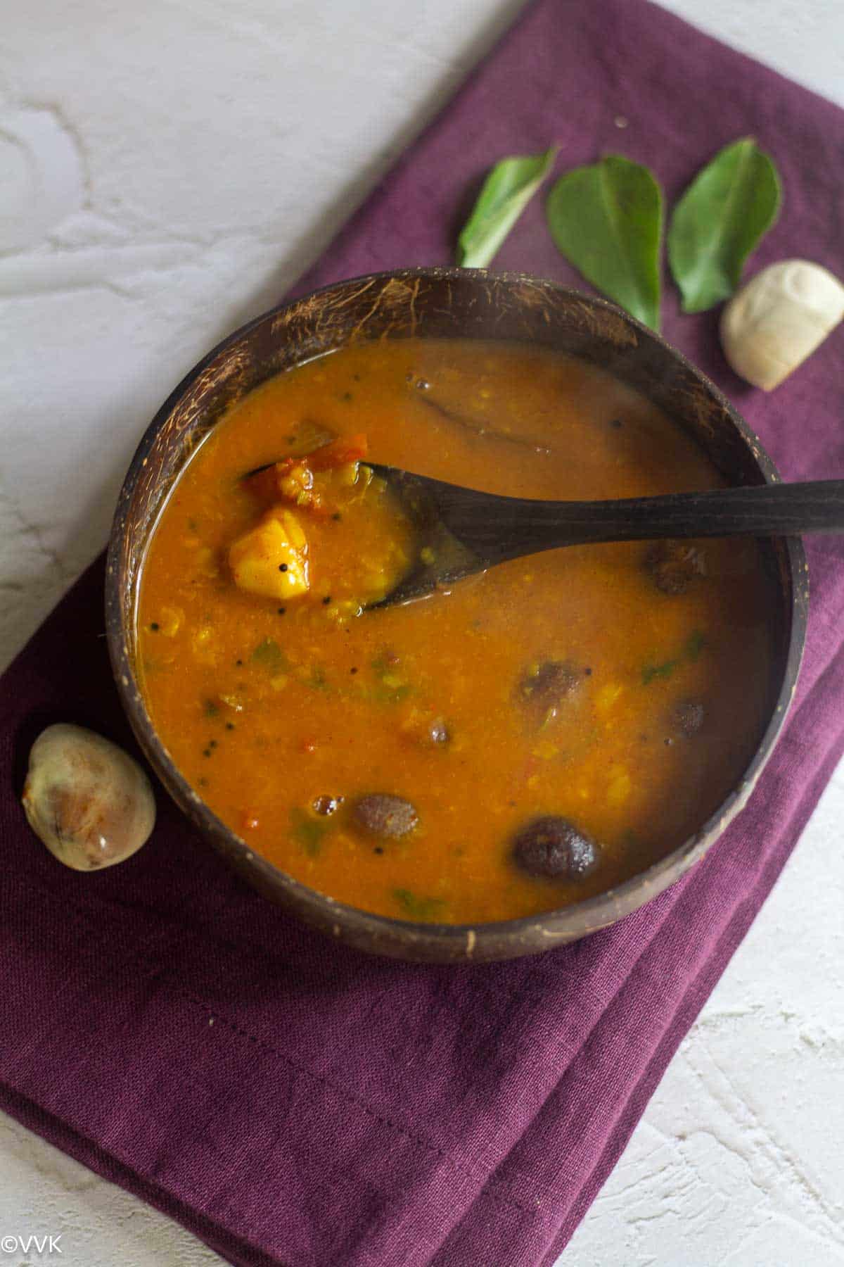 jackfruit seeds sambar served in a coconut bowl with a spoon lift which has the cooked jackfruit seeds