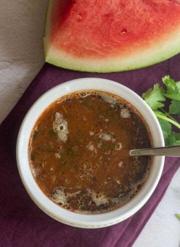 square image of watermelon rasam with melon on the side
