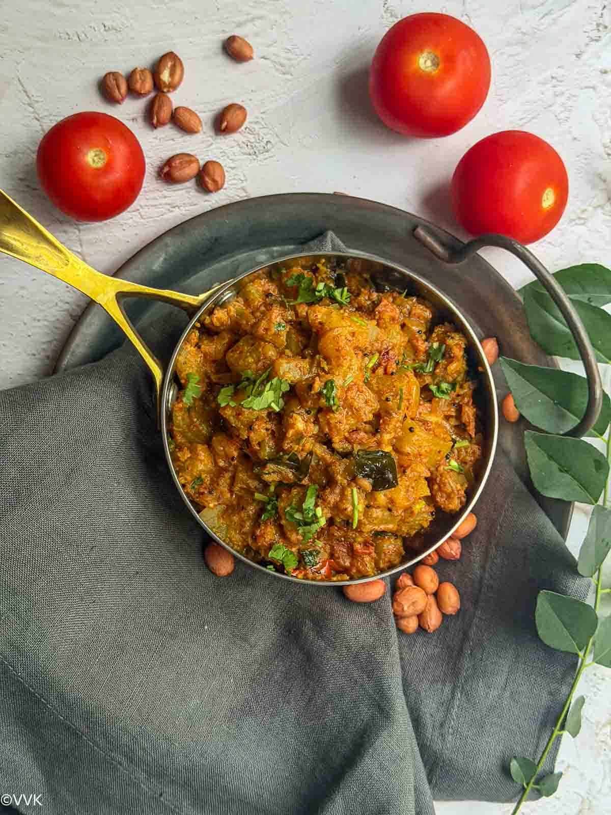 Overhead shot of bottle gourd peanut curry with tomatoes peanuts and curry leaves on the side